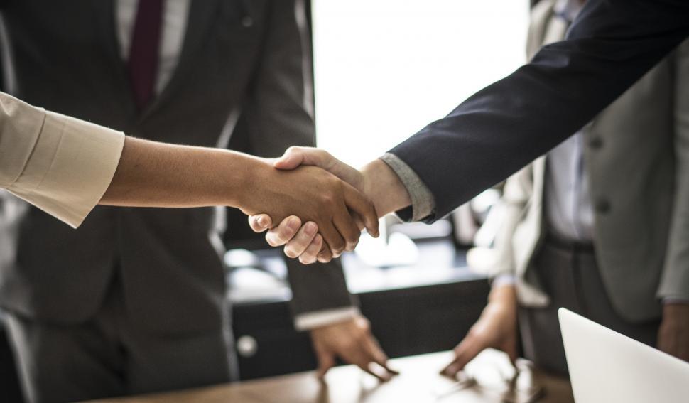 Closeup of two hands, shaking in agreement. The background indicates an office environment.